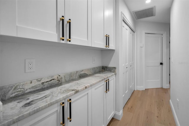 bar with white cabinets, light wood-type flooring, and light stone countertops