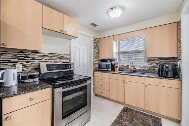 kitchen featuring sink, stainless steel appliances, tasteful backsplash, dark stone counters, and light brown cabinetry