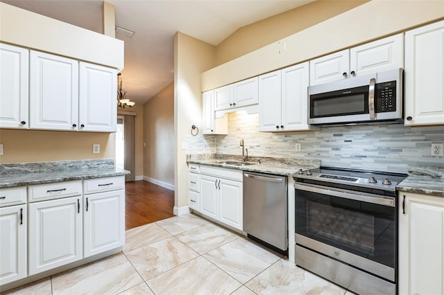 kitchen with appliances with stainless steel finishes, light stone counters, sink, white cabinets, and lofted ceiling