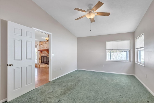 unfurnished room with a stone fireplace, ceiling fan, carpet, and vaulted ceiling