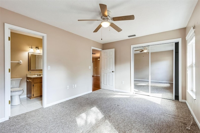 unfurnished bedroom with light carpet, a closet, ensuite bathroom, and ceiling fan