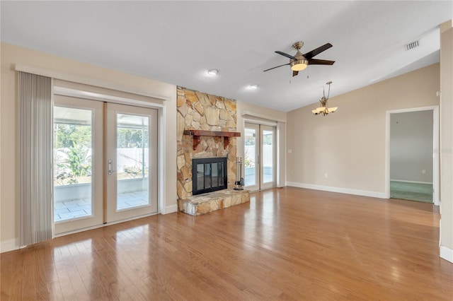 unfurnished living room featuring french doors, wood-type flooring, vaulted ceiling, a fireplace, and ceiling fan with notable chandelier