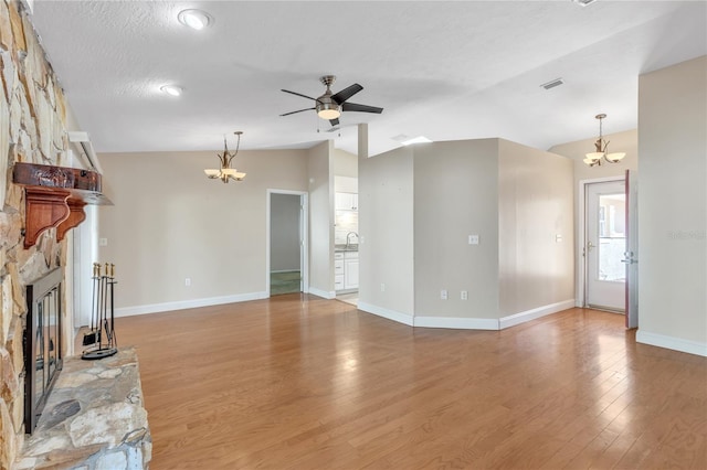 unfurnished living room with ceiling fan with notable chandelier, vaulted ceiling, sink, hardwood / wood-style floors, and a stone fireplace