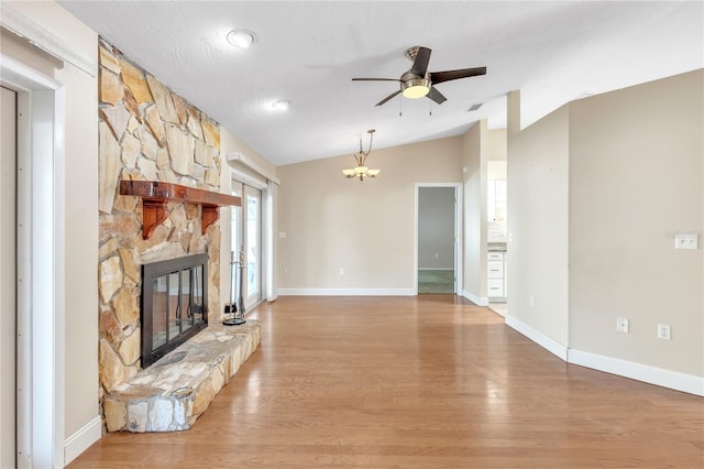 unfurnished living room featuring a stone fireplace, light hardwood / wood-style flooring, ceiling fan with notable chandelier, and vaulted ceiling