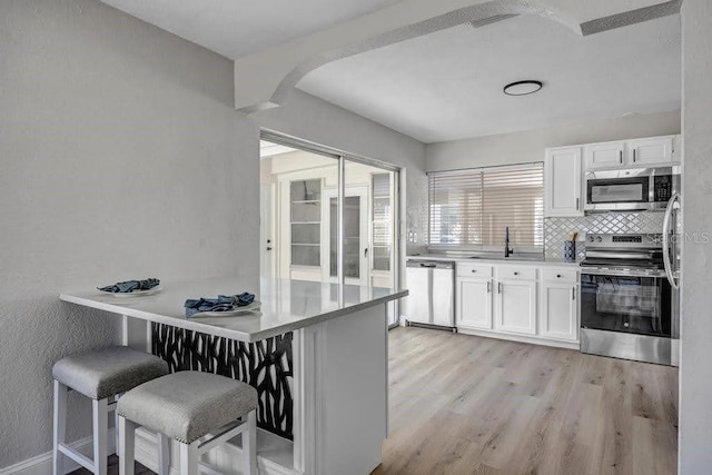 kitchen with white cabinetry, a breakfast bar, light hardwood / wood-style floors, and appliances with stainless steel finishes