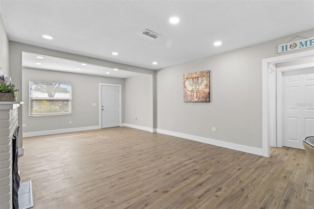 unfurnished living room with light hardwood / wood-style floors, a textured ceiling, and a brick fireplace