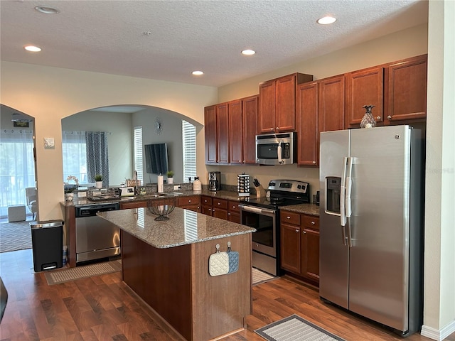 kitchen with dark wood-type flooring, kitchen peninsula, a center island, and stainless steel appliances