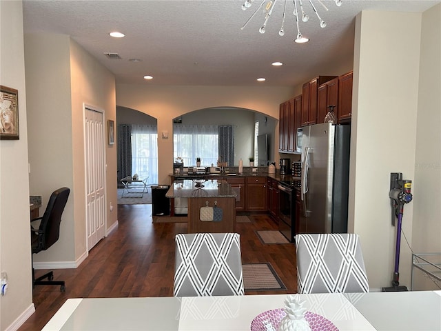 kitchen with electric stove, dark wood-type flooring, a textured ceiling, a breakfast bar area, and stainless steel fridge