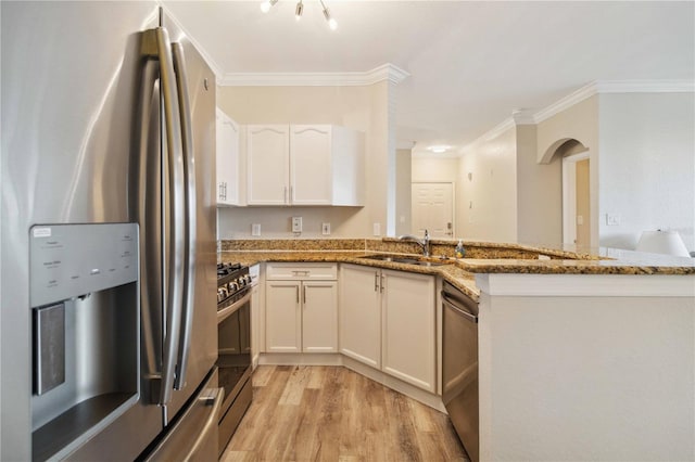 kitchen with appliances with stainless steel finishes, sink, light hardwood / wood-style flooring, dark stone countertops, and white cabinetry