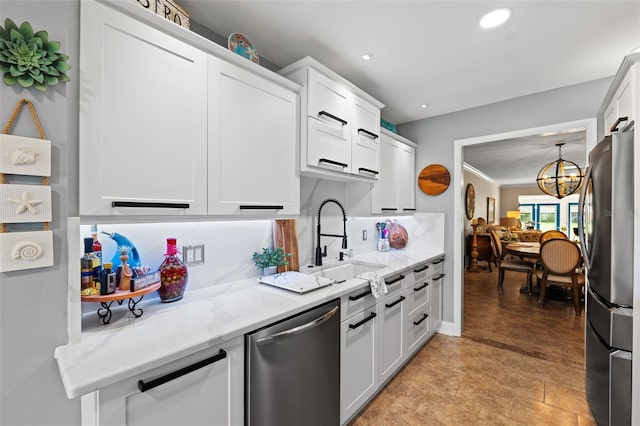 kitchen featuring light stone countertops, stainless steel appliances, sink, a notable chandelier, and white cabinets