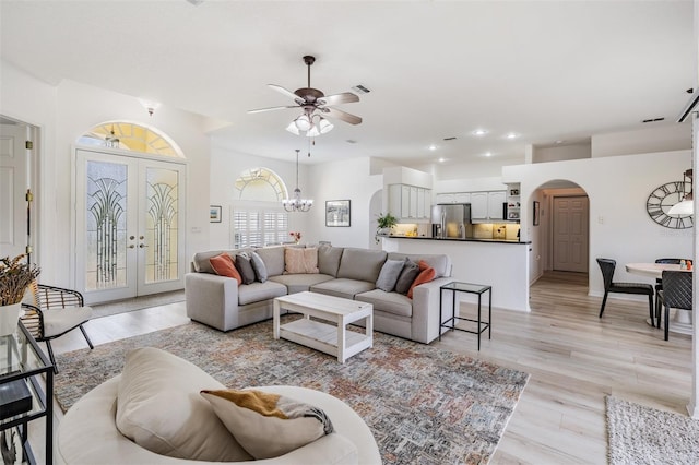 living room with french doors, ceiling fan with notable chandelier, and light wood-type flooring