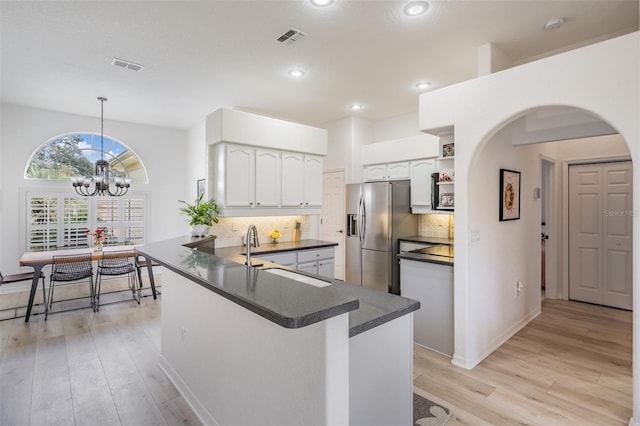 kitchen featuring kitchen peninsula, stainless steel refrigerator with ice dispenser, sink, pendant lighting, and white cabinets