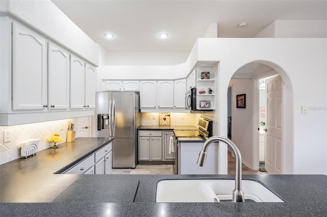 kitchen with sink, kitchen peninsula, decorative backsplash, white cabinets, and appliances with stainless steel finishes