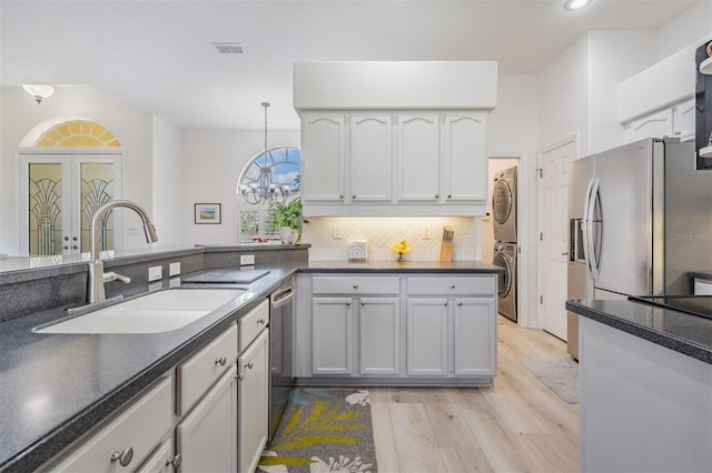 kitchen with pendant lighting, sink, light hardwood / wood-style flooring, stacked washing maching and dryer, and white cabinetry