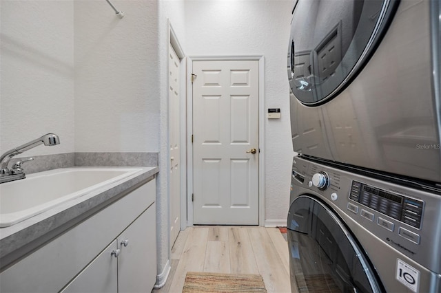 washroom with cabinets, stacked washer and dryer, light hardwood / wood-style floors, and sink