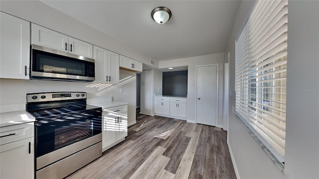 kitchen with light wood-type flooring, stainless steel appliances, and white cabinetry