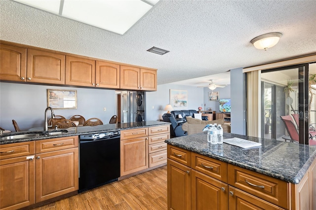 kitchen with ceiling fan, sink, black dishwasher, stacked washer and clothes dryer, and light wood-type flooring