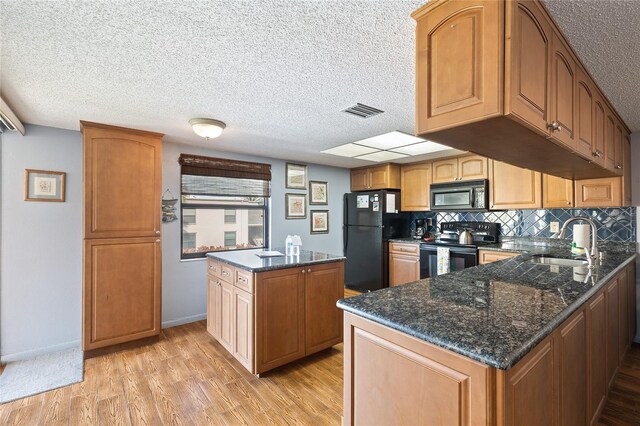 kitchen with dark stone counters, a textured ceiling, sink, black appliances, and light hardwood / wood-style flooring