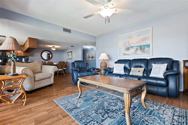 living room with ceiling fan, light wood-type flooring, and a textured ceiling