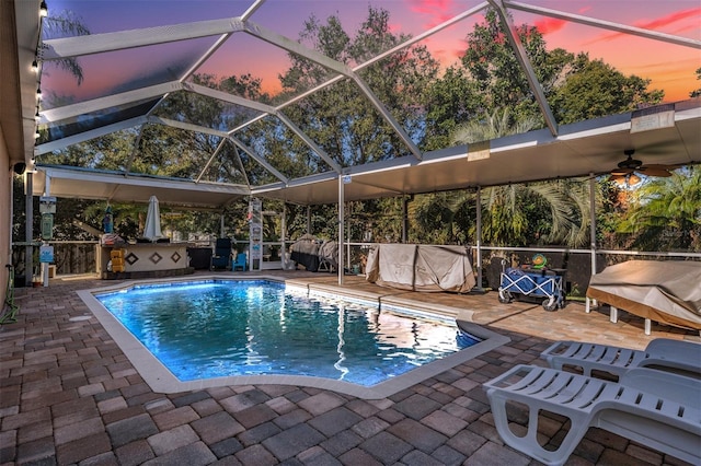 pool at dusk with a patio area and glass enclosure