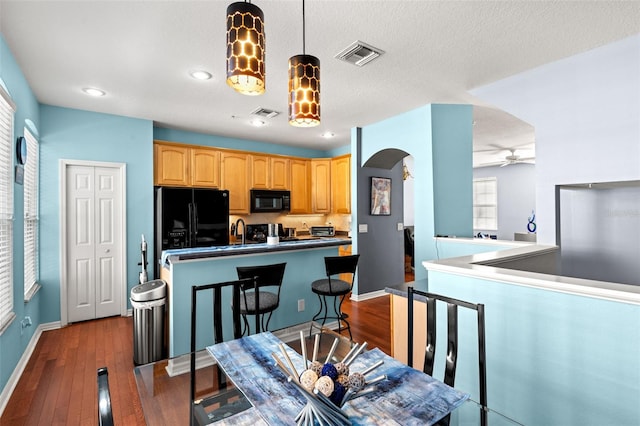 kitchen with black appliances, hanging light fixtures, kitchen peninsula, ceiling fan, and dark hardwood / wood-style floors