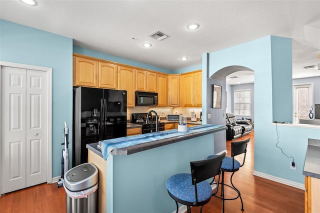 kitchen with a breakfast bar, dark wood-type flooring, black appliances, and light brown cabinets