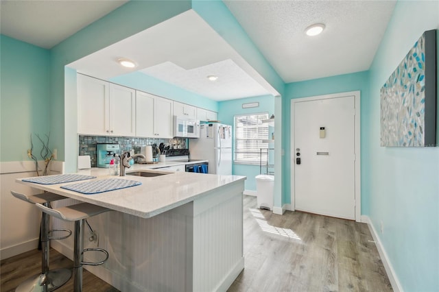 kitchen featuring kitchen peninsula, a kitchen bar, white appliances, sink, and white cabinets