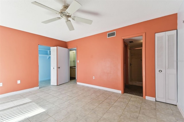 unfurnished bedroom with ensuite bath, ceiling fan, light tile patterned floors, and multiple closets