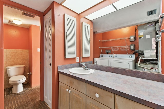 bathroom featuring vanity, tile patterned flooring, toilet, independent washer and dryer, and tile walls