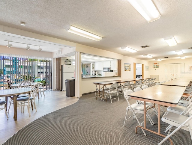 dining area featuring a textured ceiling, track lighting, light hardwood / wood-style flooring, and sink