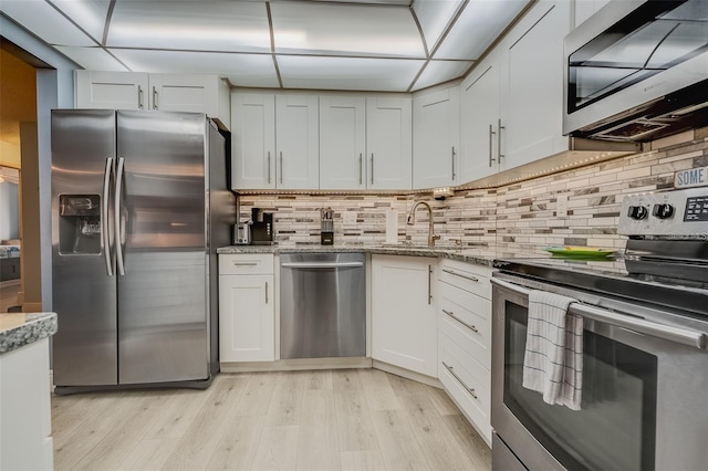 kitchen with light stone countertops, appliances with stainless steel finishes, light wood-type flooring, sink, and white cabinetry