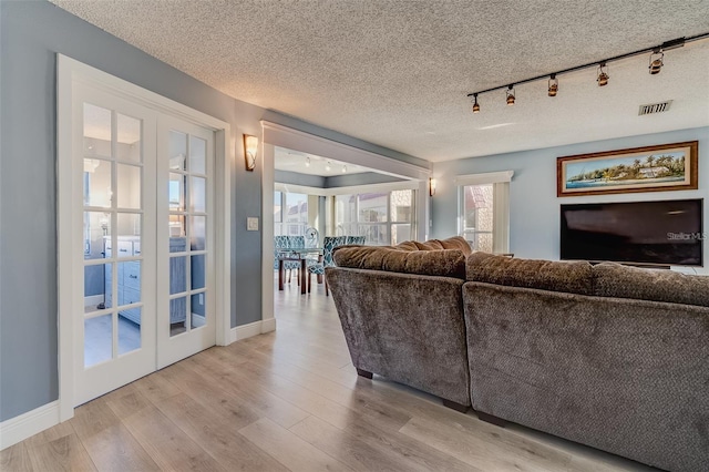 living room featuring a textured ceiling, light wood-type flooring, rail lighting, and french doors