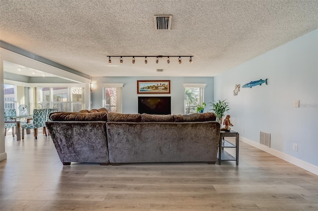 living room featuring a textured ceiling, light wood-type flooring, and track lighting