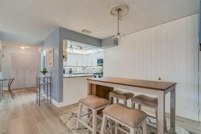 interior space with white cabinets, tasteful backsplash, decorative light fixtures, light hardwood / wood-style floors, and stainless steel appliances