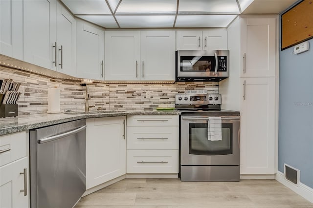 kitchen featuring white cabinetry, light stone counters, light hardwood / wood-style flooring, backsplash, and appliances with stainless steel finishes