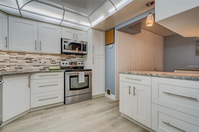 kitchen featuring white cabinets, appliances with stainless steel finishes, decorative light fixtures, and light hardwood / wood-style flooring