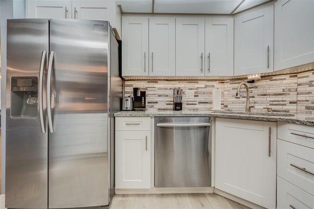 kitchen featuring white cabinets, sink, light stone countertops, light wood-type flooring, and stainless steel appliances