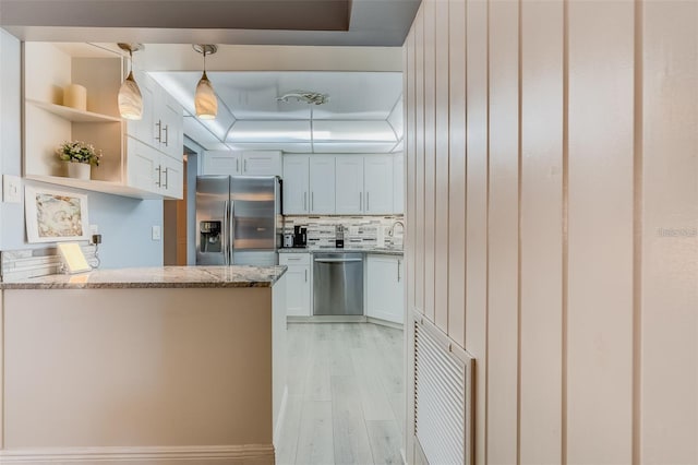 kitchen with hanging light fixtures, white cabinets, stainless steel appliances, and light hardwood / wood-style flooring