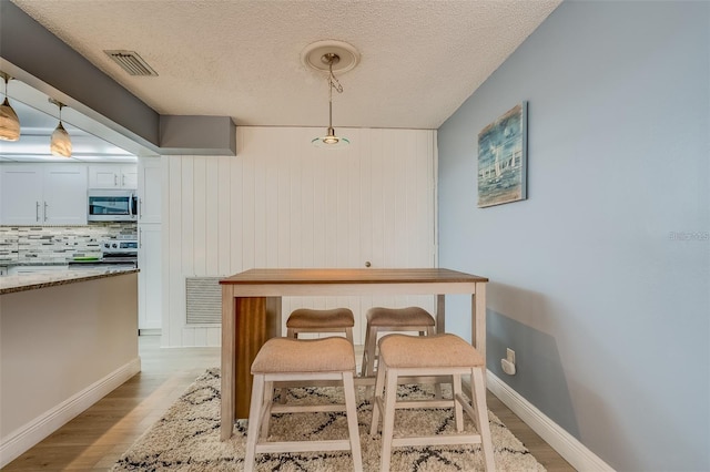 dining area featuring a textured ceiling, light wood-type flooring, and wood walls