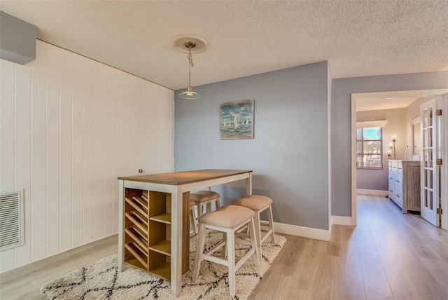 dining area with a textured ceiling, light hardwood / wood-style flooring, and wooden walls