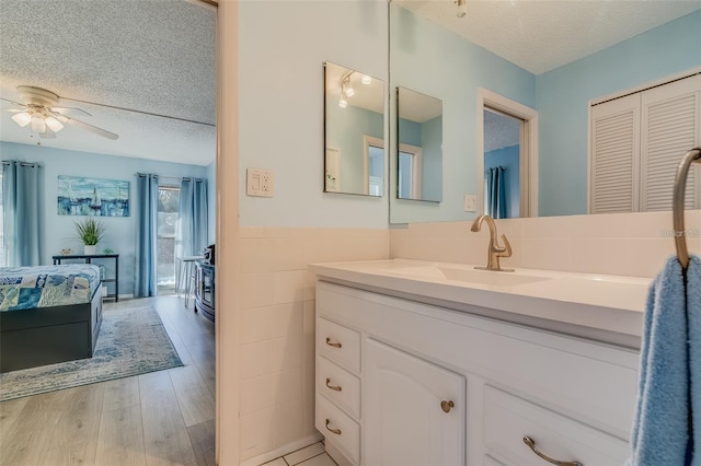 bathroom with vanity, ceiling fan, a textured ceiling, tile walls, and wood-type flooring