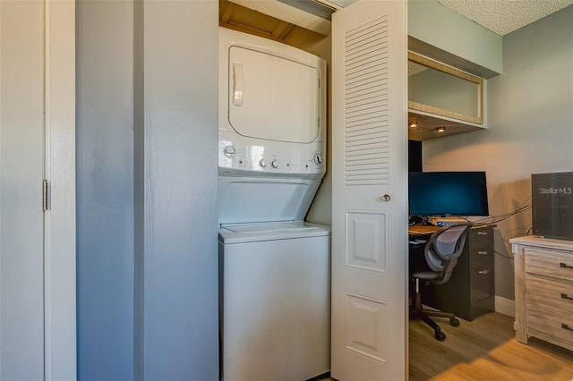 washroom with a textured ceiling, light hardwood / wood-style floors, and stacked washer and dryer