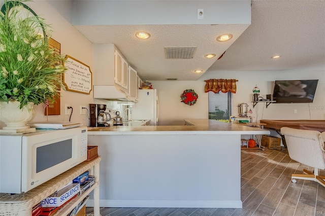 kitchen with a textured ceiling, white appliances, kitchen peninsula, and dark wood-type flooring