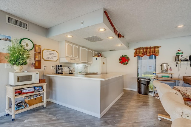 kitchen with a textured ceiling, white appliances, kitchen peninsula, and dark wood-type flooring