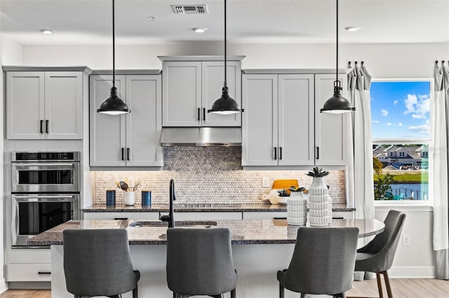 kitchen featuring pendant lighting, light stone counters, and gray cabinetry