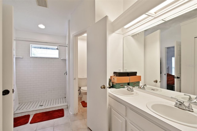 bathroom featuring toilet, vanity, tiled shower, and tile patterned floors