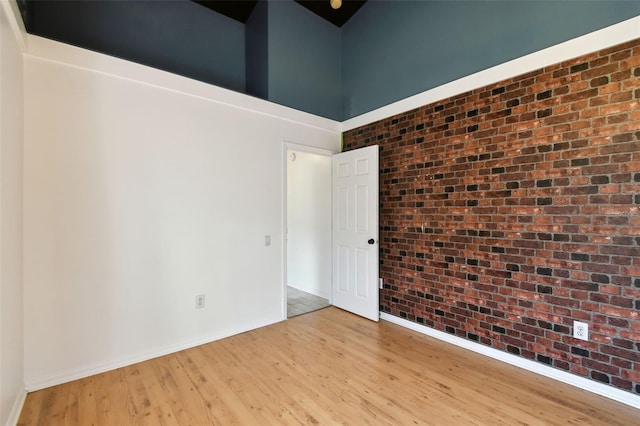 empty room with a high ceiling, brick wall, and light hardwood / wood-style flooring