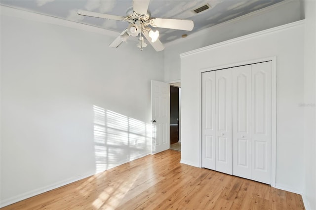 unfurnished bedroom with ceiling fan, a closet, crown molding, and light wood-type flooring