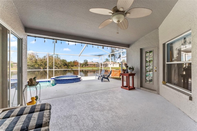 view of patio / terrace featuring ceiling fan, a water view, an in ground hot tub, and glass enclosure