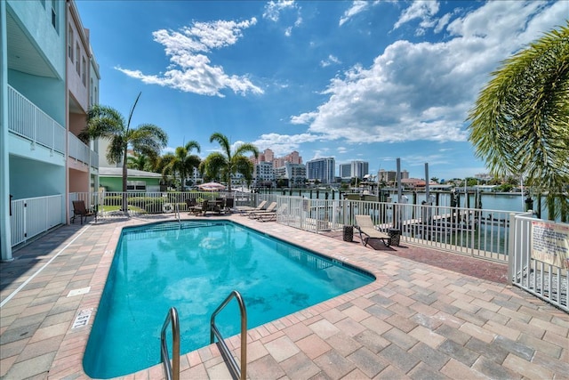 community pool featuring a view of city, a patio area, fence, and a water view